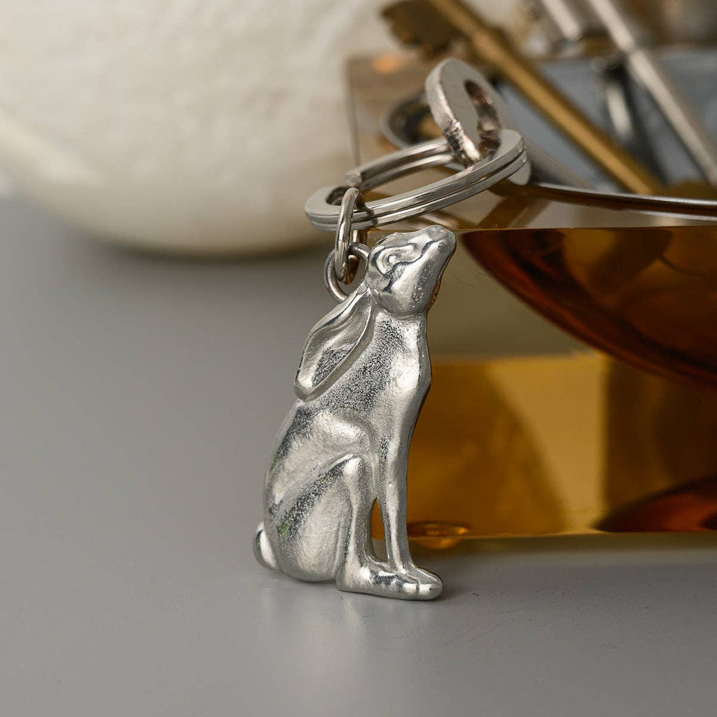 Pewter hare-shaped keychain on a reflective surface with a blurred background
