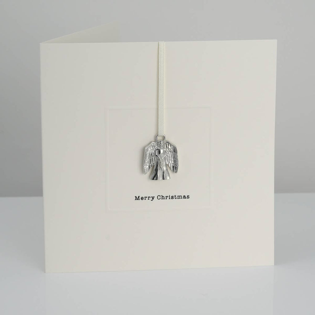 A white greeting card with a cast pewter keepsake in the shape of an angel and the words 'Merry Christmas' printed on the front.