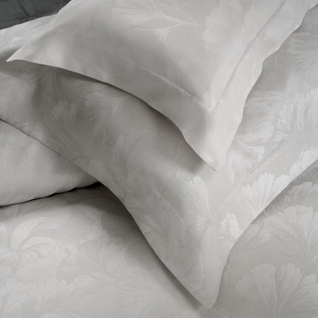 Two shams in soft white with pattern of ginkgo leaves against a folded duvet cover in same pattern