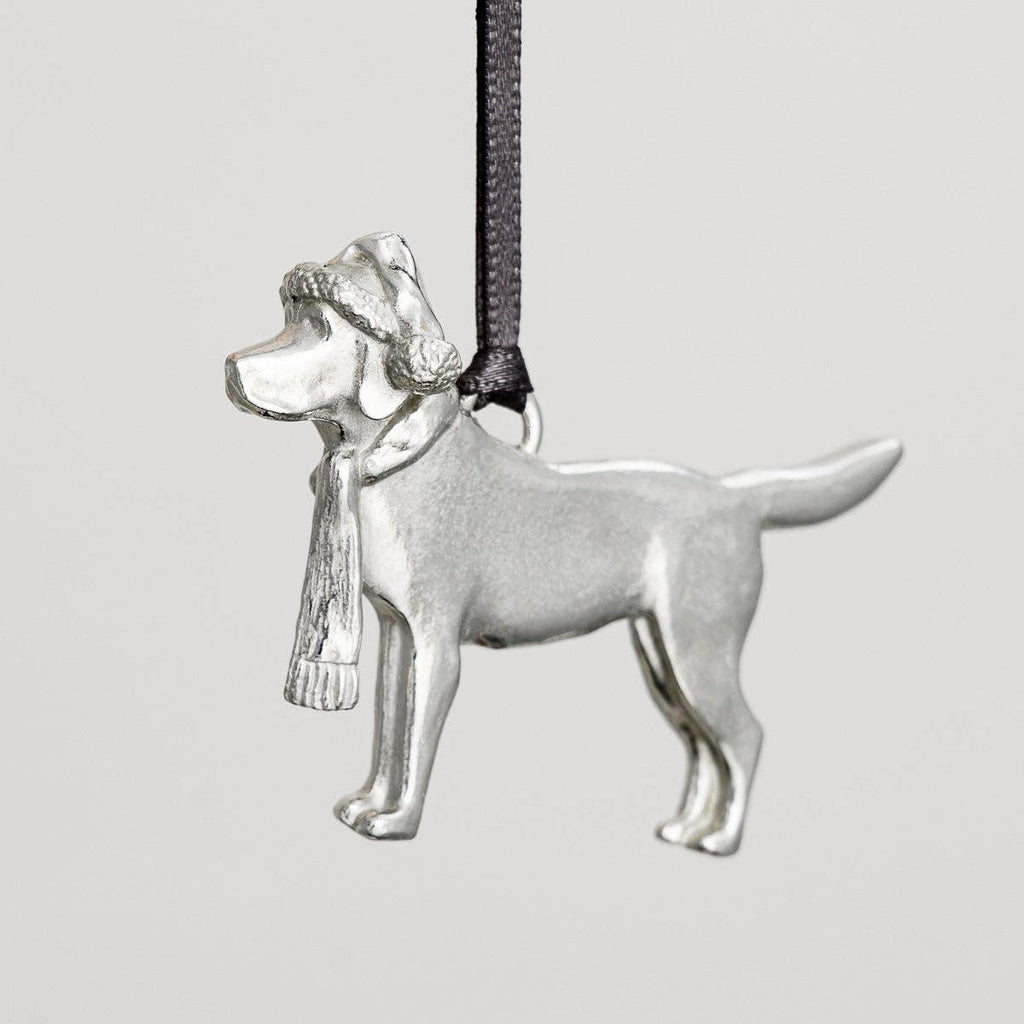 A silver-colored cast pewter decoration of a Labrador wearing a Christmas hat and scarf, suspended by a black string.