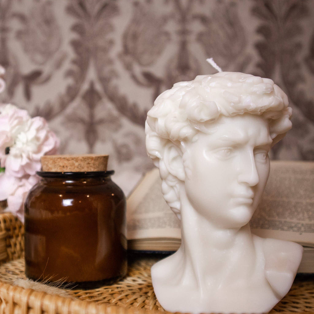 Candle shaped like a classical bust on a textured surface with decorative elements.