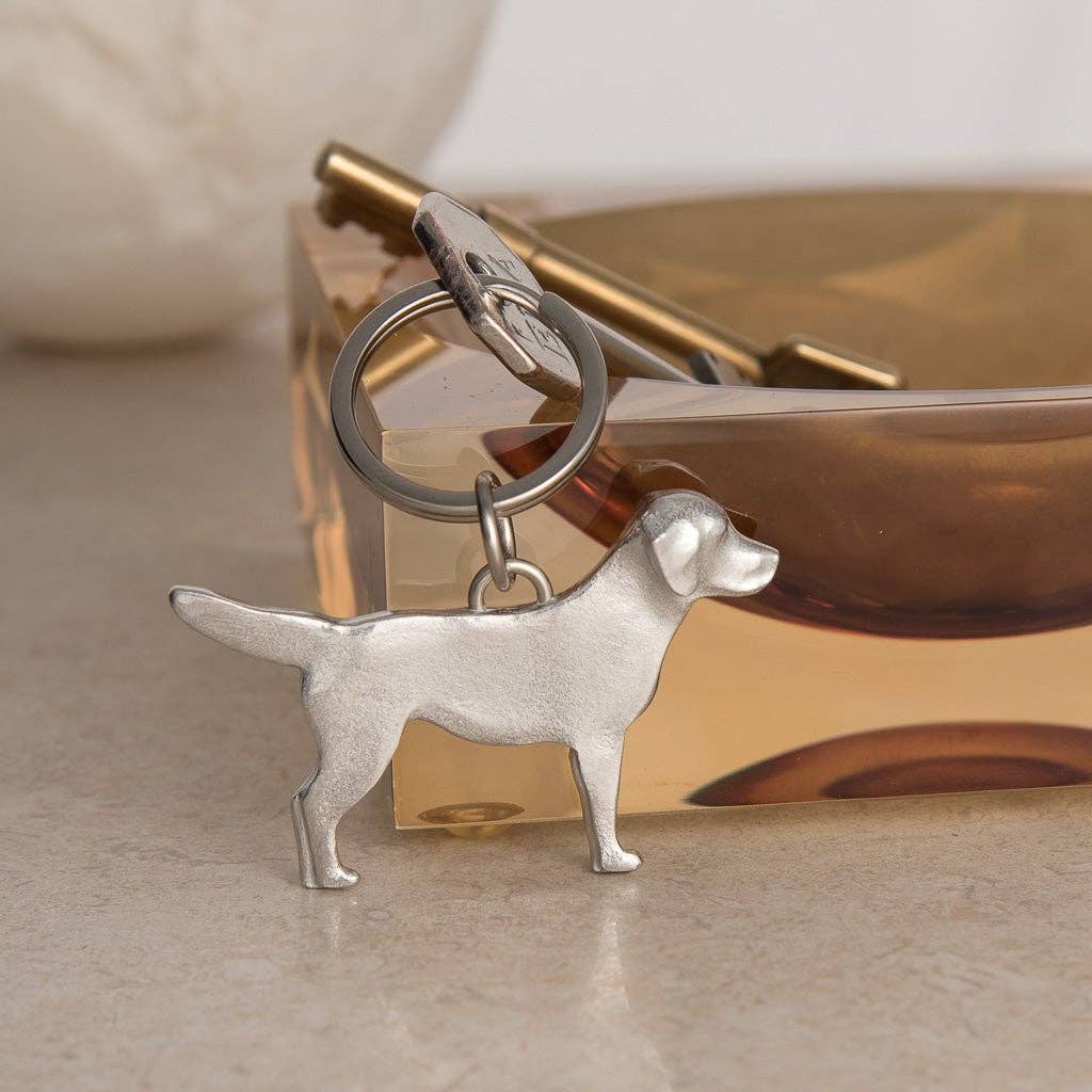 Pewter dog-shaped keychain on a beige surface with a gold tray in the background