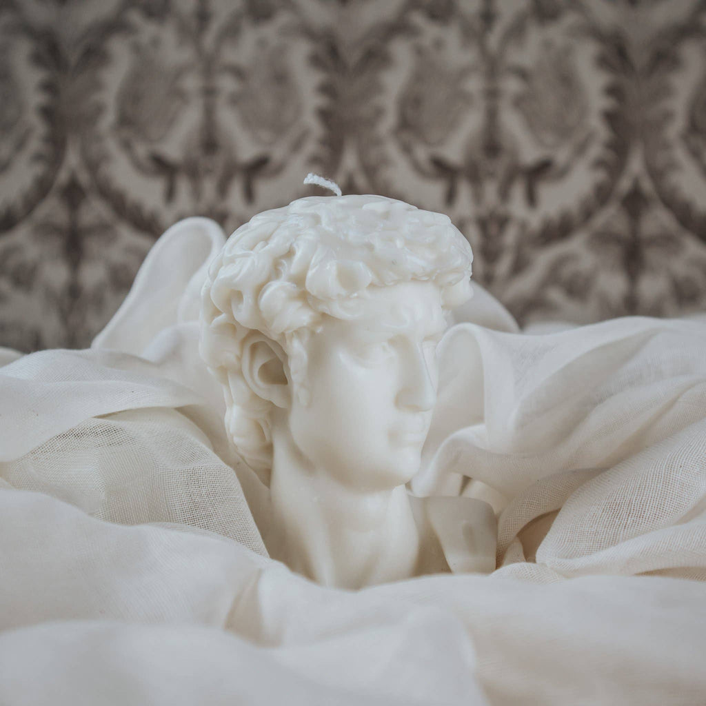 White candle bust of a classical figure against a patterned wall.