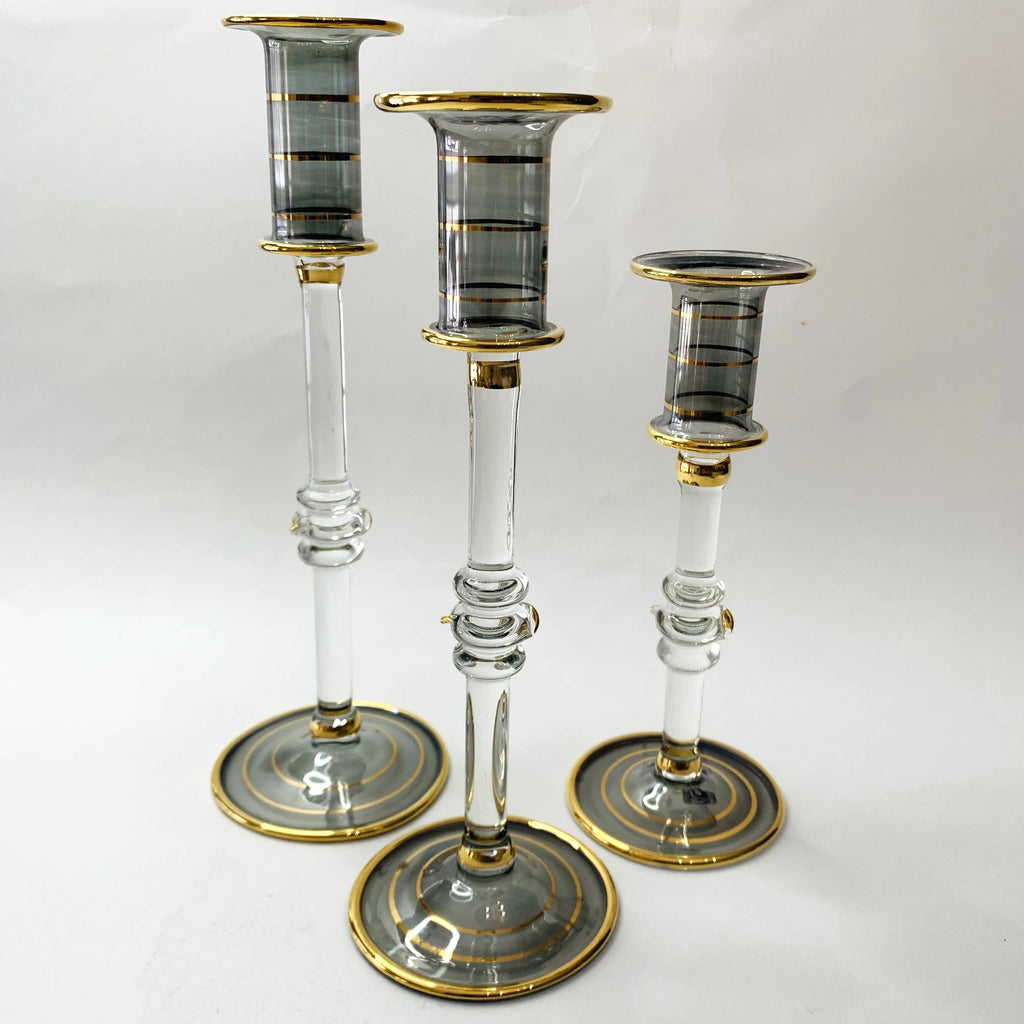 Three glass candlesticks in clear smoked glass with gold accents against a white background