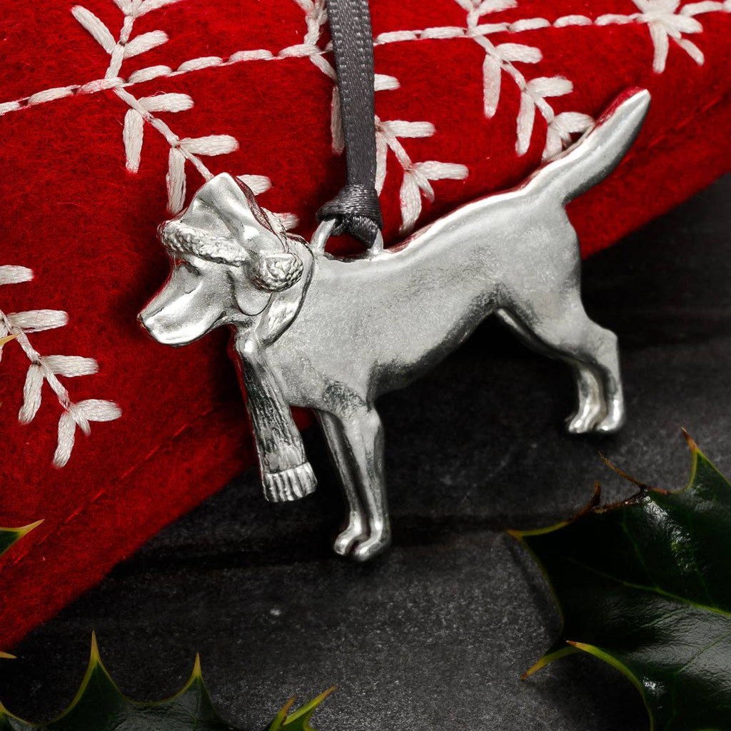 Pewter dog ornament with hat and scarf against red fabric with holly in foreground