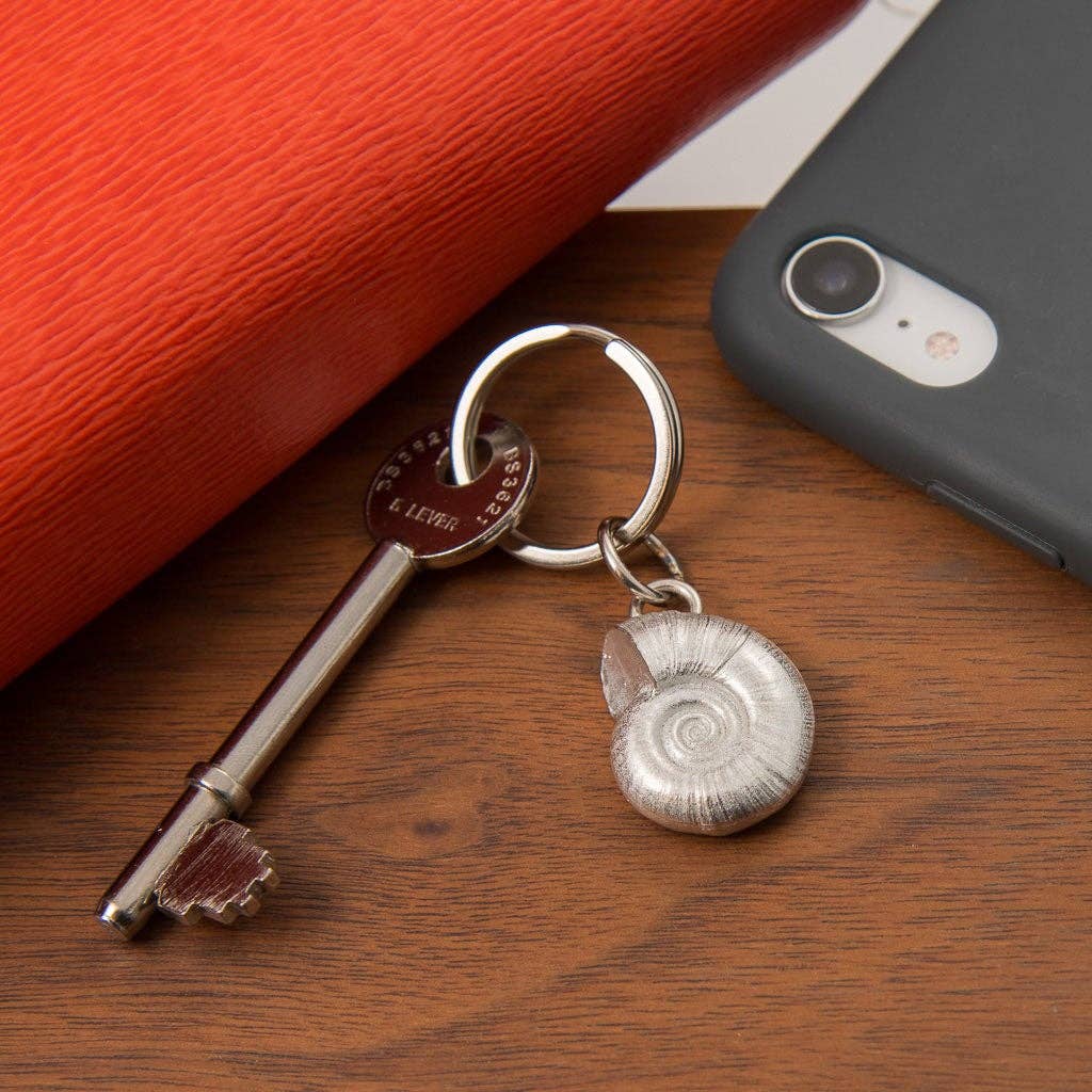 Keychain with a shell pendant on a wooden surface next to a phone