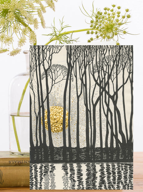 Greeting card with black and cream outlines of trees reflected in water and a hand glittered gold sunset behind.