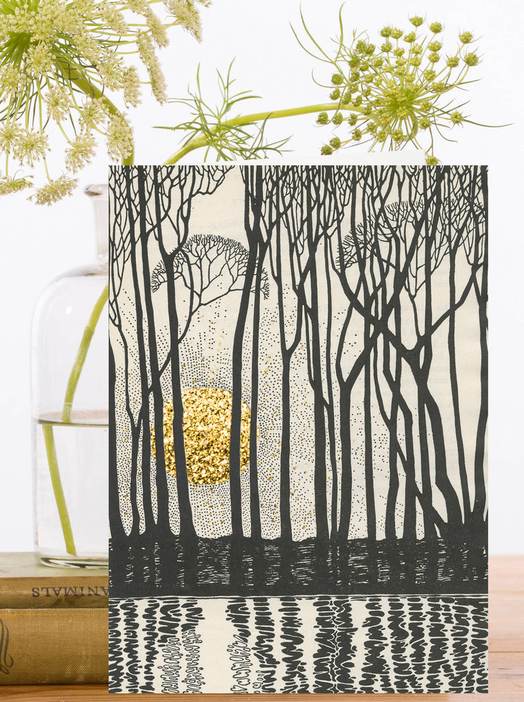 Greeting card with black and cream outlines of trees reflected in water and a hand glittered gold sunset behind.