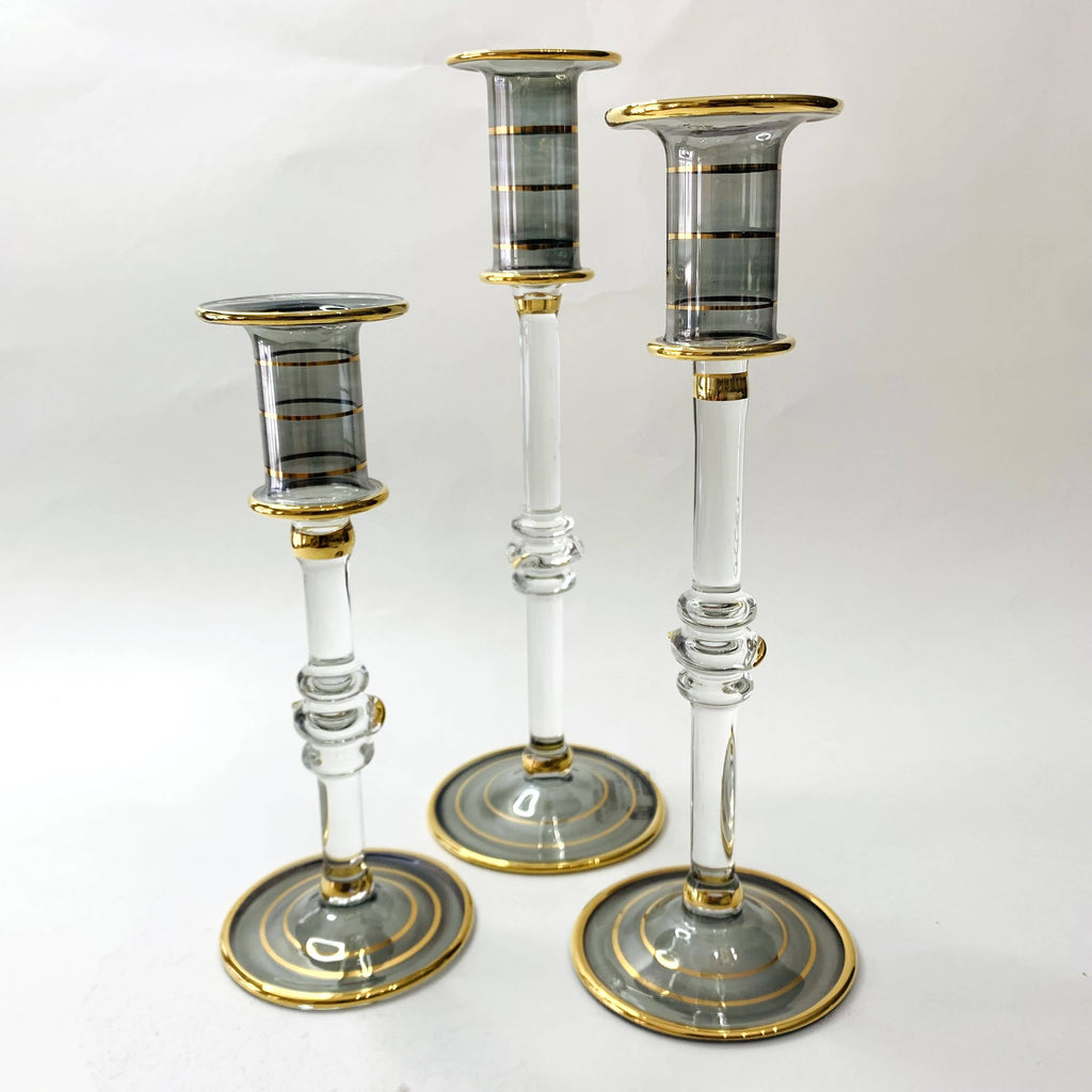 Three glass candlesticks in clear smoked glass with gold accents against a white background
