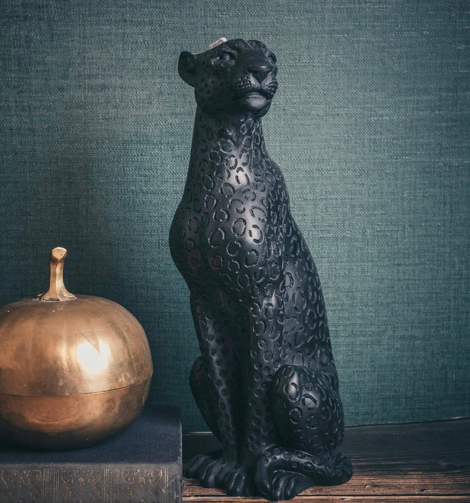 Decorative black leopard candle next to a metallic pumpkin against a textured green wall.