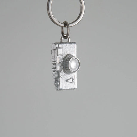 Silver camera-shaped keychain on a gray background