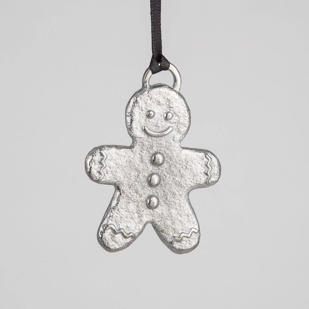 A pewter gingerbread man decoration with a happy facial expression, hanging from a ribbon and a metal chain against a gray background