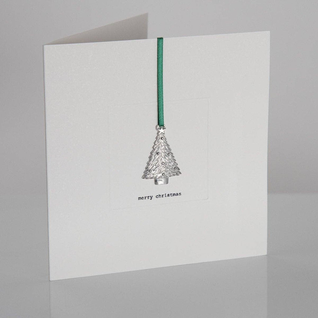 A greeting card with a white background featuring a cast pewter keepsake in the shape of a Christmas tree, with a green ribbon and a personalized message that reads 'Merry Christmas'.