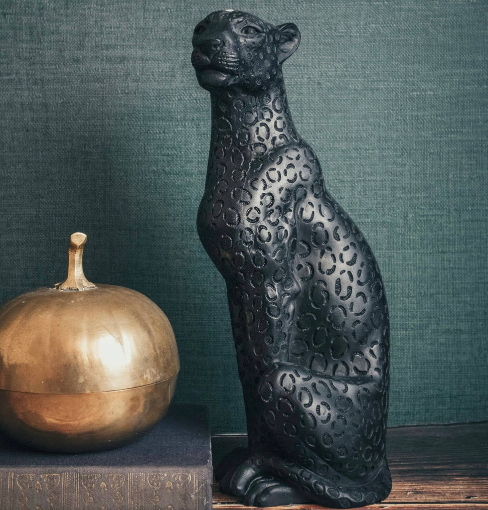 Decorative black panther candle next to a gold pumpkin on a wooden surface with a green textured background.