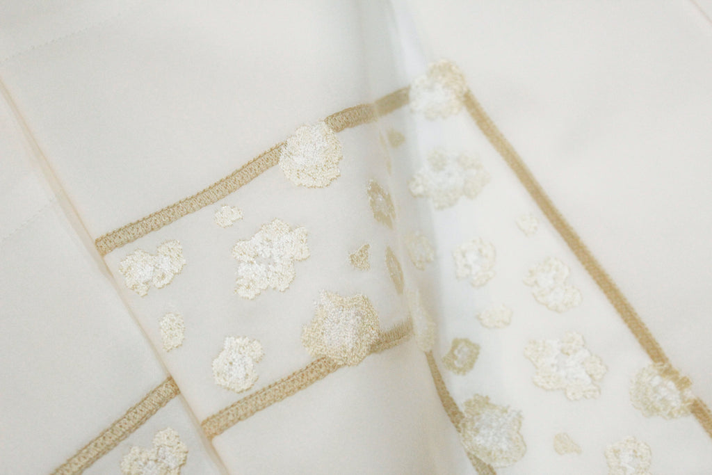 Close-up of an Ivory cotton fabric with muted gold embroidery details on the flat sheet. The frame embroidery captures the fine leopard patterns