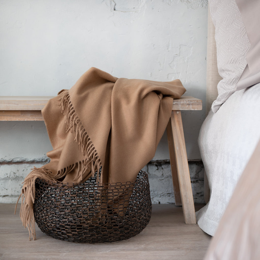 Alfie Camel Throw draped on bench with rustic basket underneath