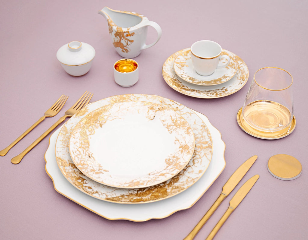 Elegant table setting with gold and white dishes on a pink background