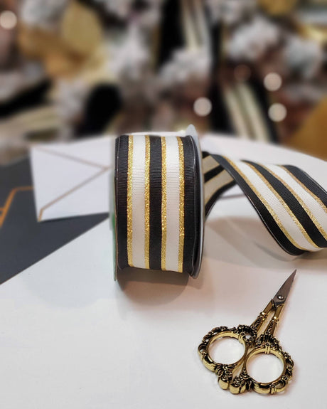 Black and white woven ribbon with gold accents and a pair of scissors on a white surface.