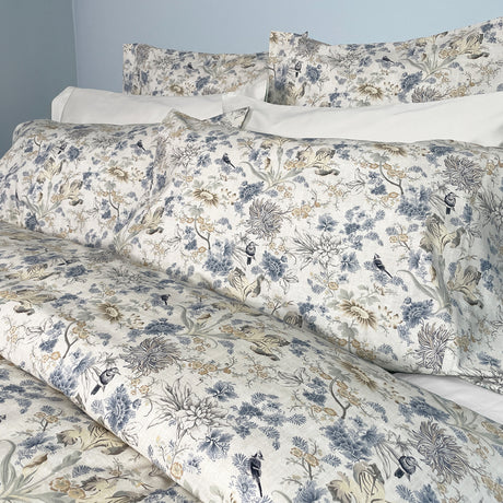 Floral and bird patterned bedding set on a bed with white pillows.