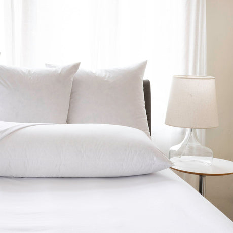 White pillows set on a bed with a lamp in the background