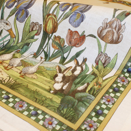 Italian tea towel that illustrates bunnies and ducks in a garden with flowers and a checkered border