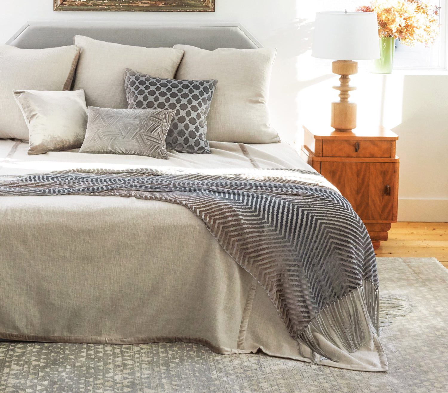 Bed with side table on right hand side. Bed has Biscotti Chunky Woven Coverlet and three matching 30" shams  in back, and three smaller accent pillows in front. A velvet throw is draped on the end of the bed.