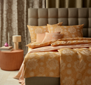 Bedroom with a bed featuring orange and beige patterned bedding, a brown headboard, and a side table with a lamp.