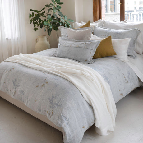 Bedding in blue with ochre tones and white accents on a bed in a sunny bedroom