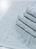 A stack of crystal blue Tuscan towels with a leaf and dot curved embroidery detail.