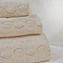 A stack of beige Tuscan towels with a leaf and dot curved embroidery detail.