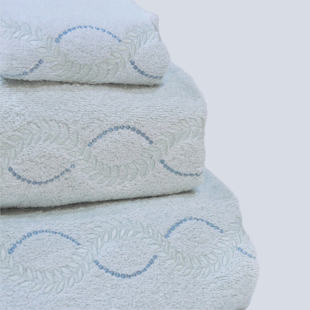 A stack of crystal blue Tuscan towels with a leaf and dot curved embroidery detail.