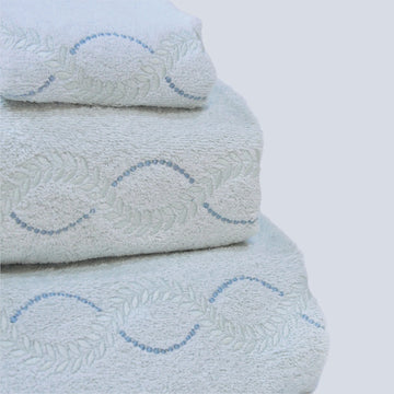 A stack of crystal blue Tuscan towels with a leaf and dot curved embroidery detail.