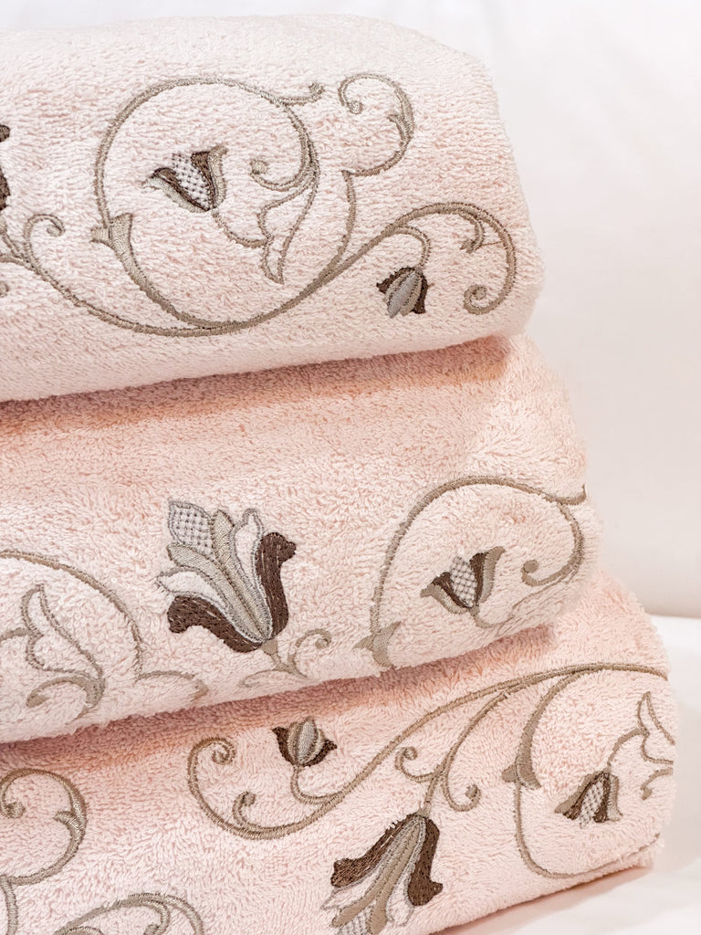 A stack of pink Tuscan towels with a flower and vine curved embroidery detail.