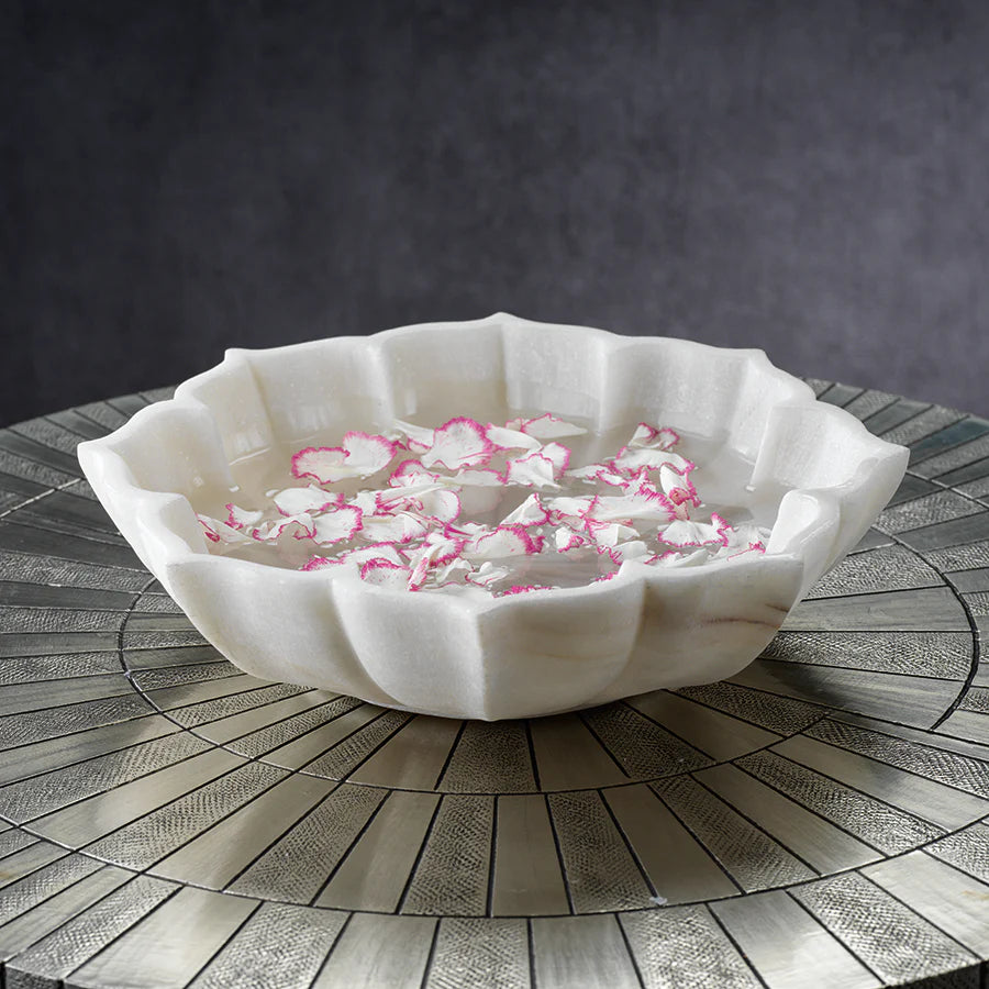Lotus marble bowl filled with water and floating petals on table with radiant circular design.