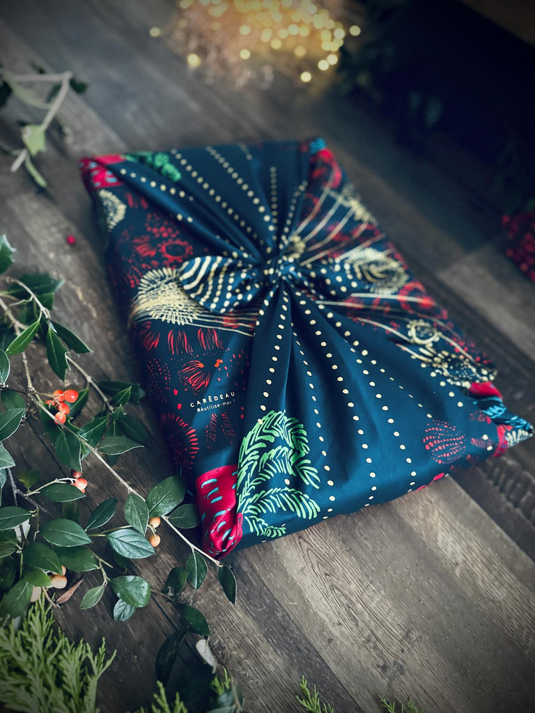 Fabric giftwrap with intricate patterns on a wooden surface with greenery.