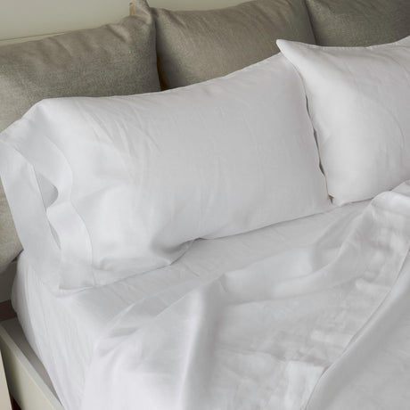 White bedding set including a fitted sheet, pillowcases, and two pillows on a bed with gray pillows in the background.