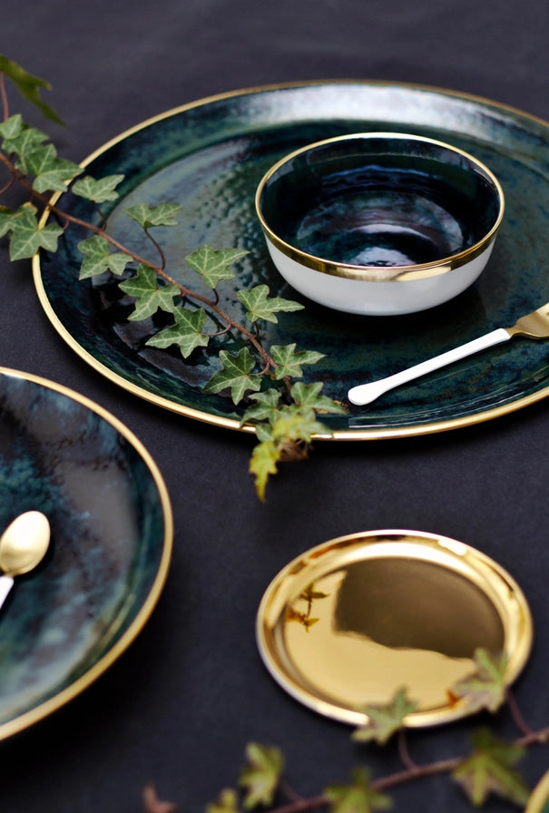 Set of dark green ceramic plates with gold rims on a dark surface.