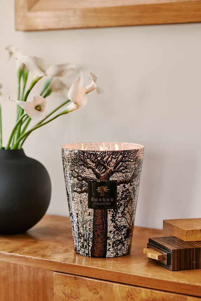 Morondo Max 24 Candle shown on wooden sideboard with vase with lilies on left
