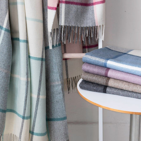 Plaid blankets in various colors draped over a chair and stacked on a small table.