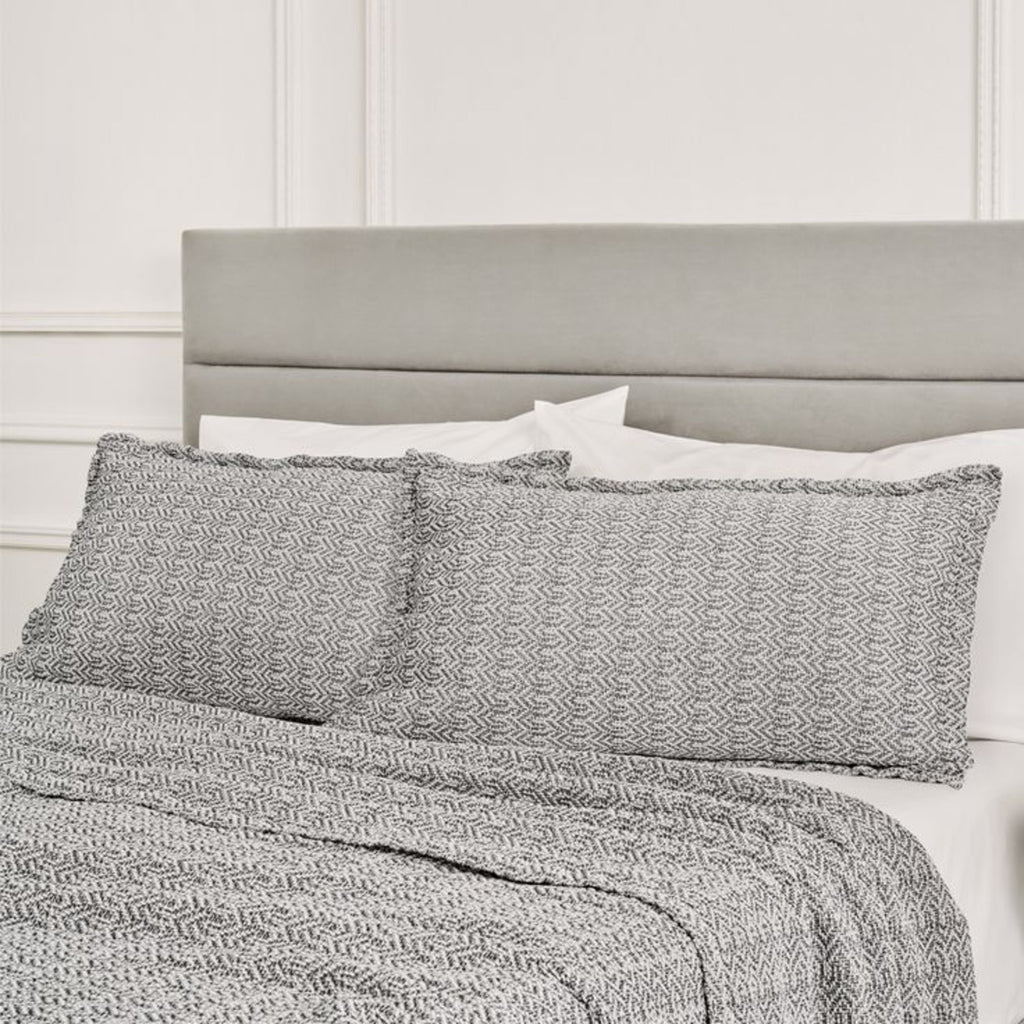 Mirage Marine coverlet and shams with interwoven graphic design on bed with white sheets and pillowcases