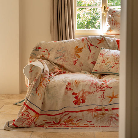 Floral-patterned blanket draped over a sofa in a room with a window and curtains.