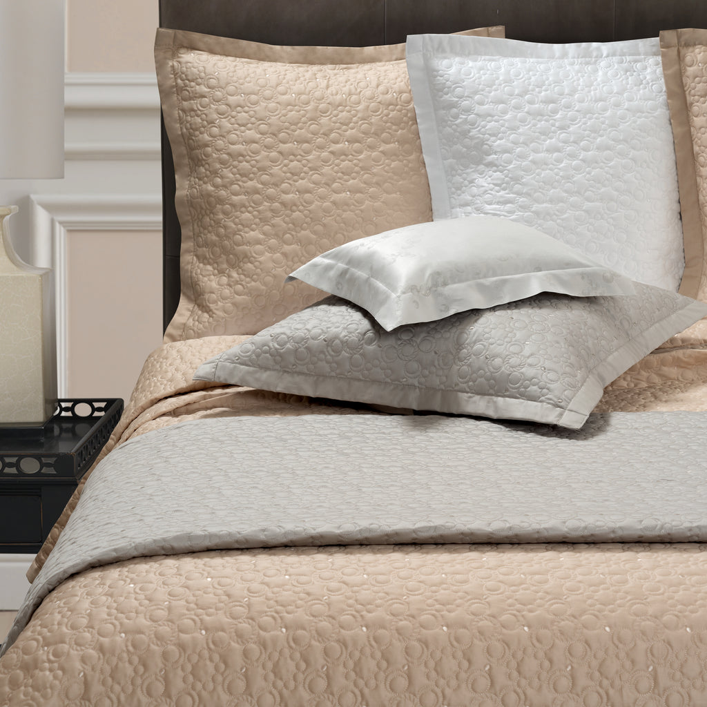 Quilted bedding set with beige, white, and gray pillows on a bed.