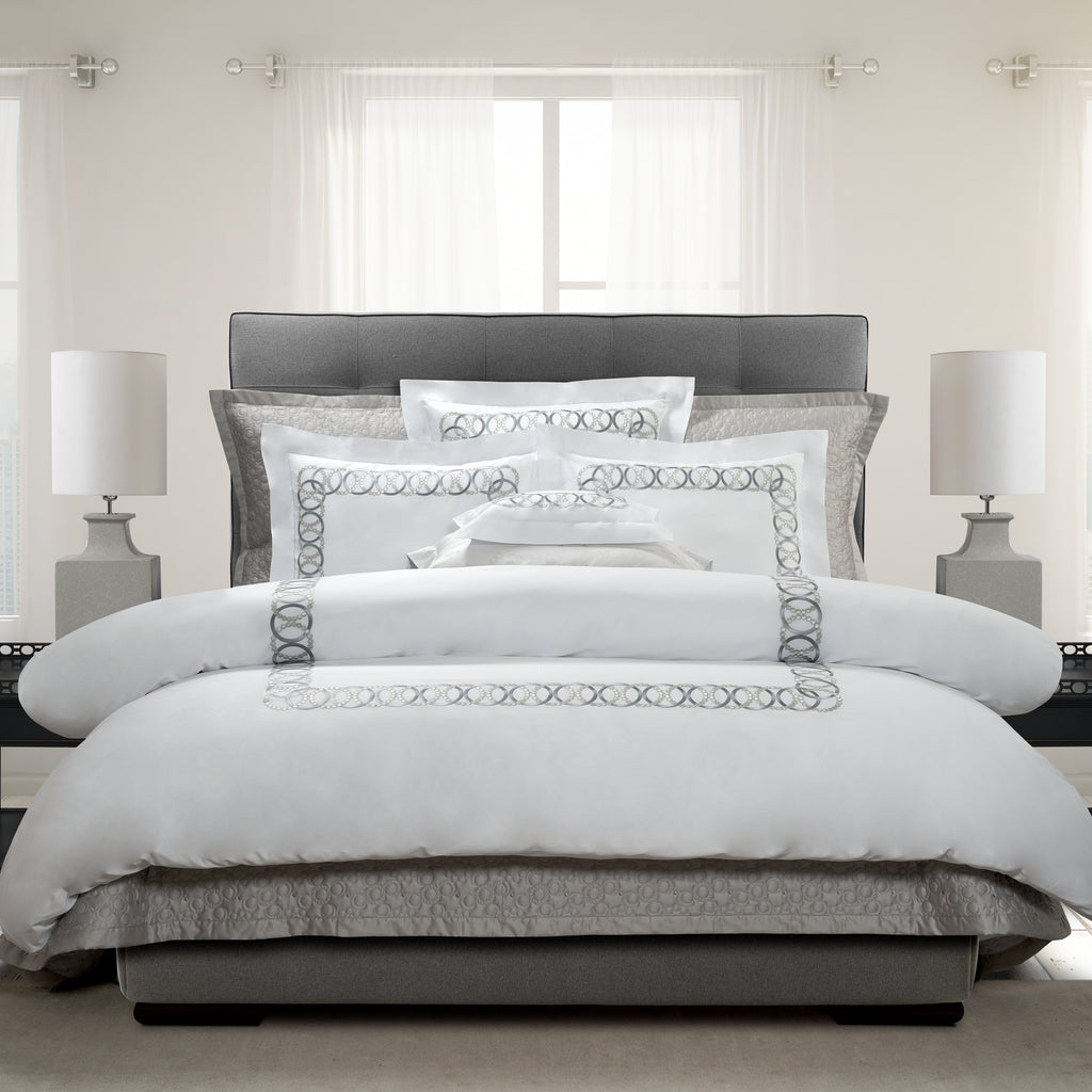 Neatly made bed with decorative pillows and a gray headboard in a well-lit room.