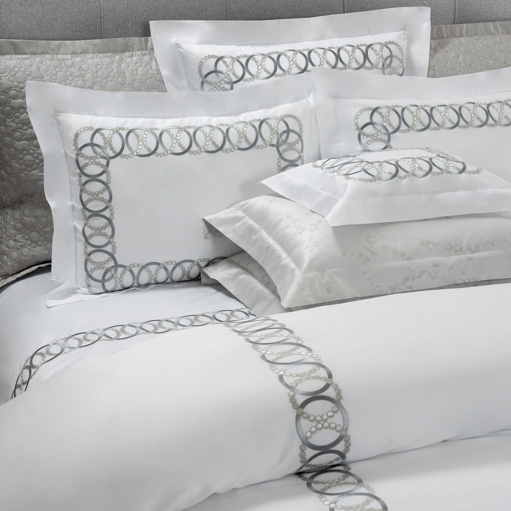 White bedding set with decorative gray embroidered patterns on a bed.