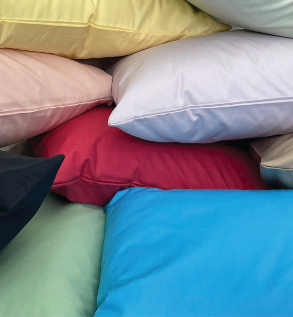A range of brightly coloured pillowcases on pillows piled on top of one another.