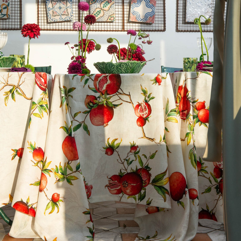 Tablecloth with pomegranate design on a table with flowers and plates.