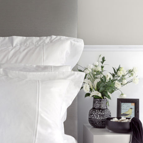 White bedding with a vase of flowers on a nightstand