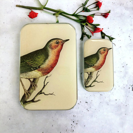Small and large rectangular tins with a bird illustration held by a hand 