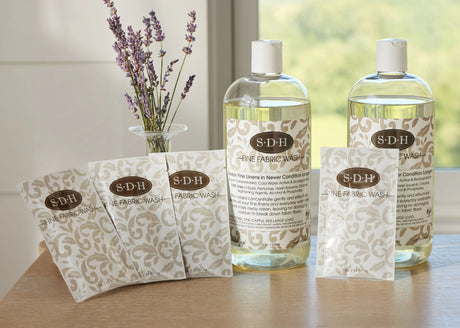 Two bottles of SDH fabric wash and several sample packets on a wooden surface with a vase full of lavender.