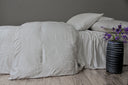 Neatly made bed with light-colored bedding with a tone on tone design and pillows against a gray wall.